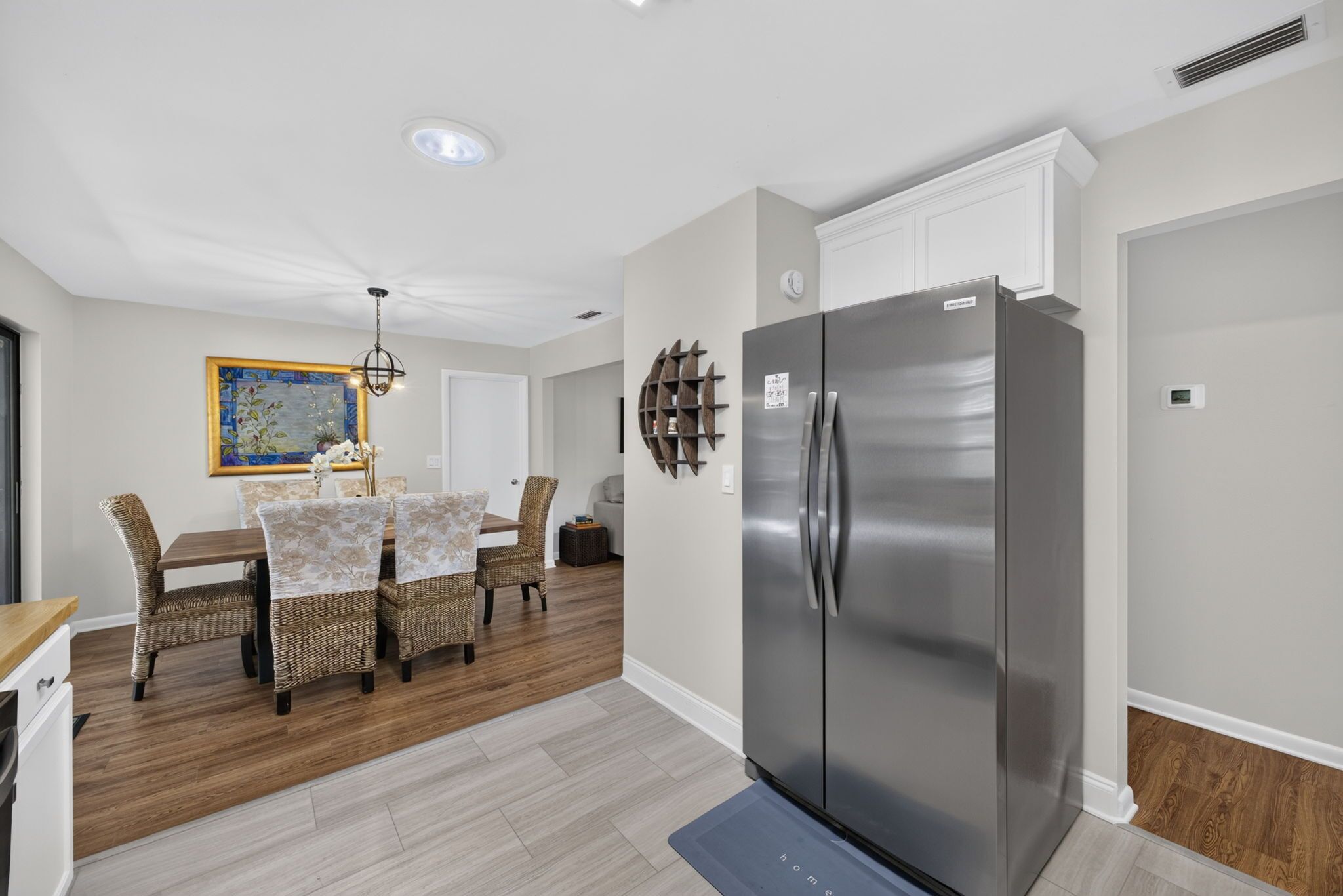 Une cuisine moderne avec un réfrigérateur en acier inoxydable, une table à manger avec des chaises en osier et un élément décoratif mural.