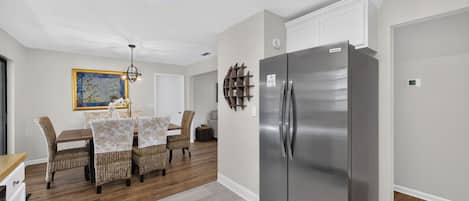 A modern kitchen with a stainless steel refrigerator, a dining table with wicker chairs, and a decorative wall piece.