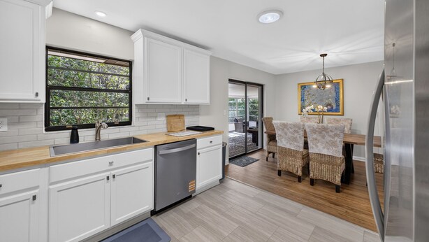 A modern kitchen with white cabinetry, a dishwasher, and a dining area with wicker chairs. - Historic Downtown Ocala Haven~Peaceful~Near WEC~Fenced~Dogs Ok~Sleeps 8 (Ocala)