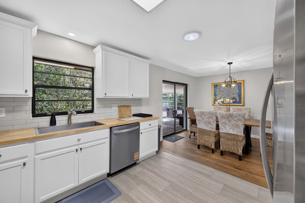 A modern kitchen with white cabinetry, a dishwasher, and a dining area with wicker chairs.