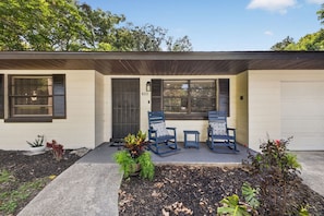 A two-story house with a front porch, two rocking chairs, and a garage.