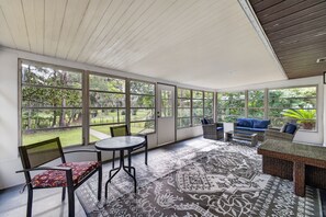 A sunroom with a large glass door, a round table, two chairs, a sofa, and a patterned rug.