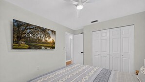 A bedroom with a bed, a wardrobe, a ceiling fan, and a wall-mounted picture. - Historic Downtown Ocala Haven~Peaceful~Near WEC~Fenced~Dogs Ok~Sleeps 8 (Ocala)