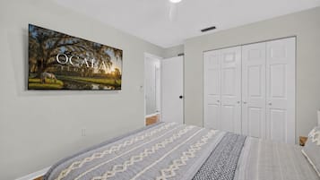A bedroom with a bed, a wardrobe, a ceiling fan, and a wall-mounted picture.
