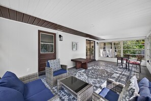 A covered patio area with wicker furniture, a patterned rug, and a view of greenery outside.