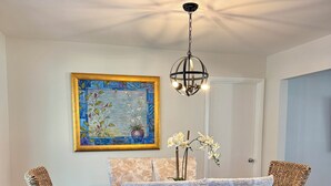 A dining area with a wooden table, wicker chairs, a floral painting, and a hanging light fixture. - Historic Downtown Ocala Haven~Peaceful~Near WEC~Fenced~Dogs Ok~Sleeps 8 (Ocala)