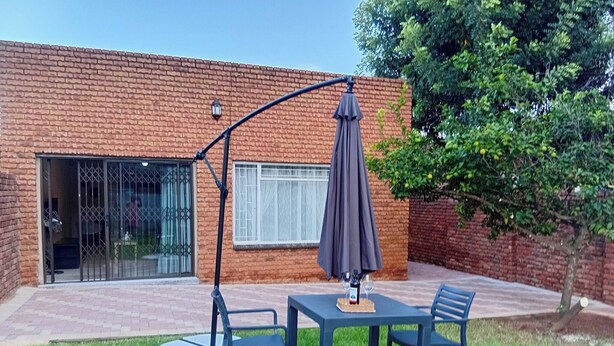 Une terrasse avec une table et des chaises, un parasol et un bâtiment en briques doté d’une porte-fenêtre coulissante.
