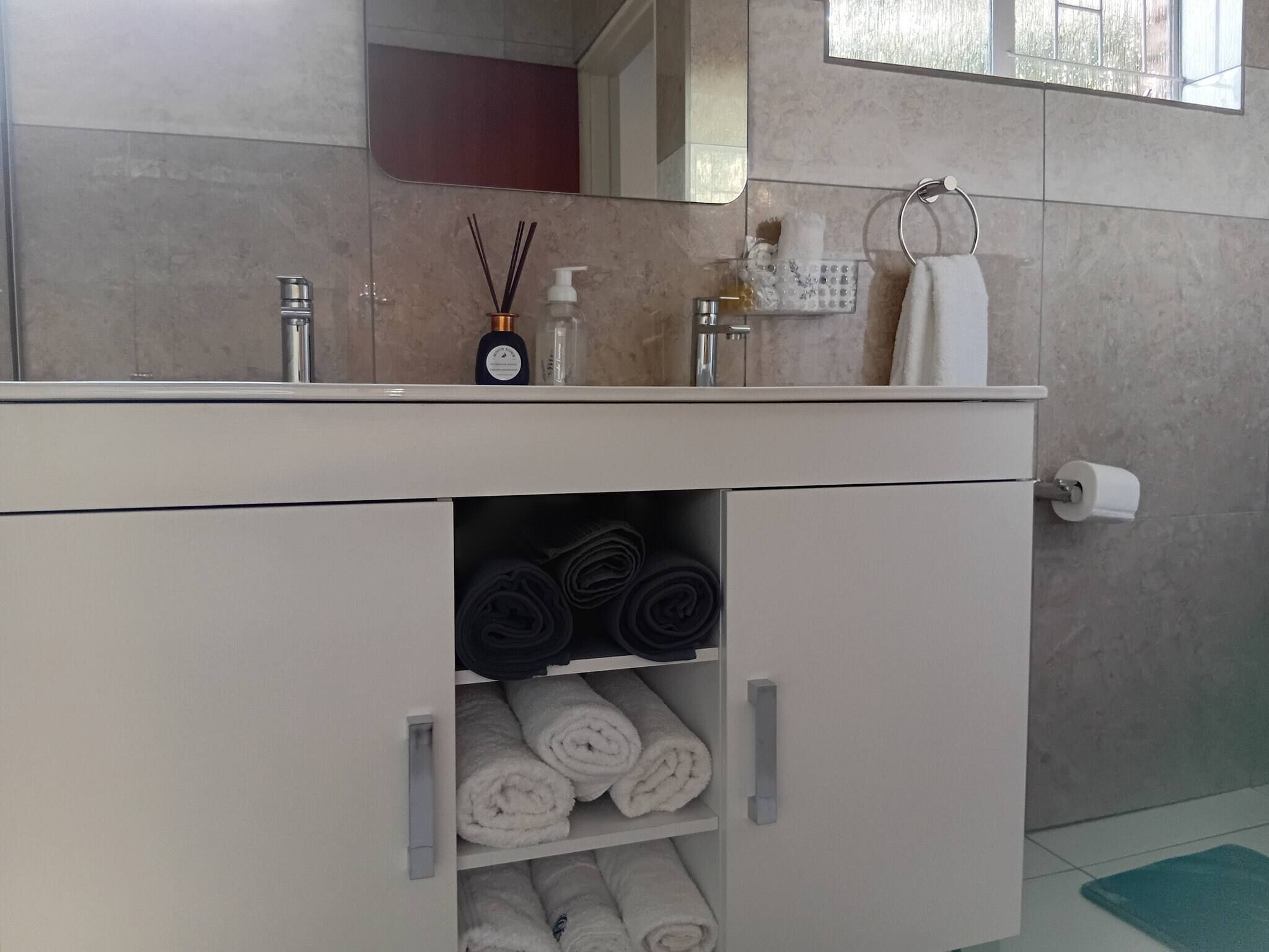 Un baño con tocador blanco, un espejo, un perchero y una repisa con toallas enrolladas.