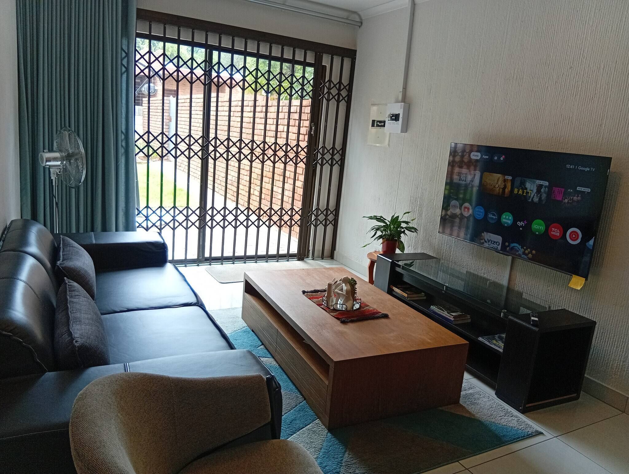 A living room with a sofa, coffee table, TV, and a view through a barred window.