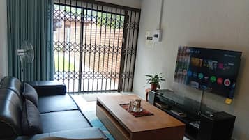 A living room with a sofa, coffee table, TV, and a view through a barred window.