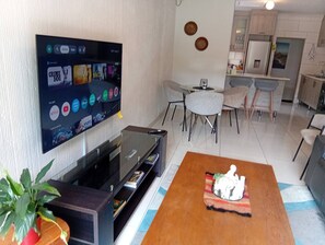 A modern living room with a flat-screen TV, a coffee table, and a dining area with chairs and a table. - Executive Garden Flat in Plk (Polokwane)