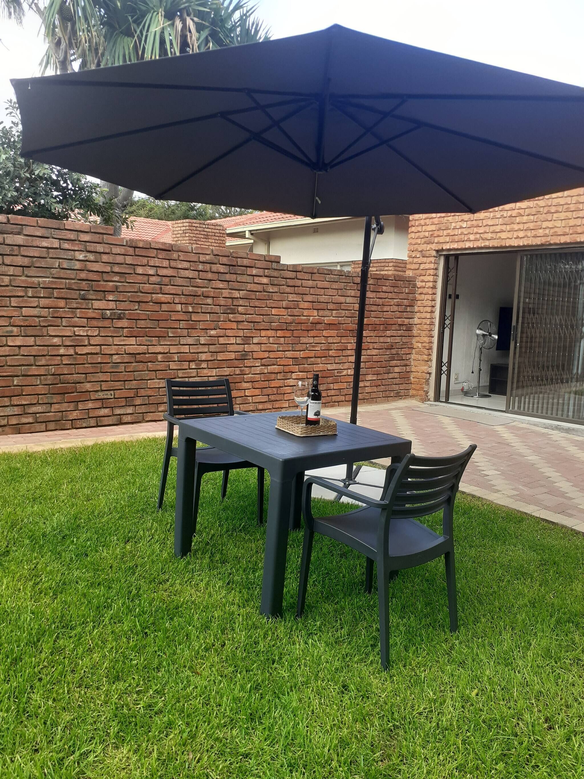 Un patio con una mesa, sillas, un paraguas grande y un muro de ladrillo.