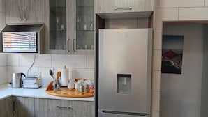 Une cuisine équipée d’un réfrigérateur en acier inoxydable, de meubles de rangement en bois et d’une fenêtre avec des stores.