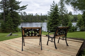 A wooden deck with two benches facing a lake surrounded by trees.