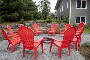A circular arrangement of red chairs around a fire pit on a gravel surface, with a house and trees in the background. - Spacious Madawaska River Cottage with Hot Tub, Games Room & Dock (Brudenell, Lyndoch and Raglan)