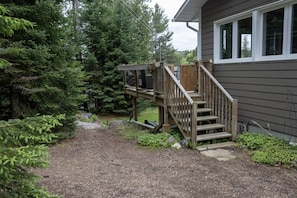 A wooden deck leading to a house with a gravel path and surrounding greenery. - Spacious Madawaska River Cottage with Hot Tub, Games Room & Dock (Brudenell, Lyndoch and Raglan)