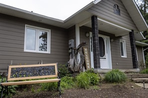 A house with a porch, a welcome sign, and a bench. - Spacious Madawaska River Cottage with Hot Tub, Games Room & Dock (Brudenell, Lyndoch and Raglan)