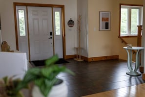 A room with a wooden floor, a white door, a small table with a decorative item, and a window with a view of greenery.