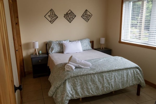 A neatly made bed with a green patterned bedspread, two bedside tables with lamps, and decorative wall art above the bed.