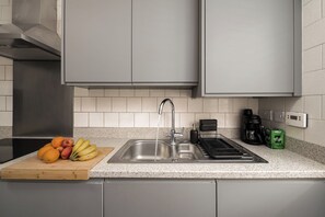 Eine Küche mit Spüle aus Edelstahl, einer Kaffeemaschine und einem Schneidebrett mit Orangen und Bananen.