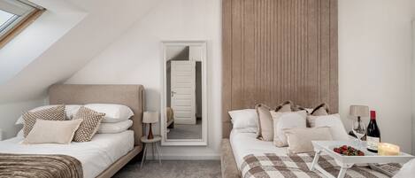 Une chambre d’hôtel moderne avec deux lits, une grande fenêtre, un luminaire au plafond et une table de chevet sur laquelle se trouvent une bouteille et une bougie.
