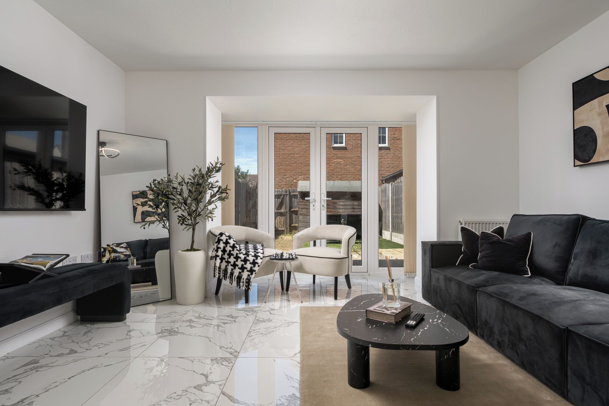 Una sala de estar moderna con piso de mármol, un sofá negro, un sillón blanco y una mesa de centro.