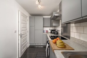 Een moderne keuken met grijze kastjes, een roestvrijstalen afzuigkap en een aanrecht met fruit en een waterkoker.