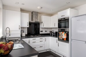 A modern kitchen with white cabinetry, a stainless steel range hood, a built-in oven, and a refrigerator. - Chic 4BR Home | Garden | Free Parking | Maidstone (Kent)