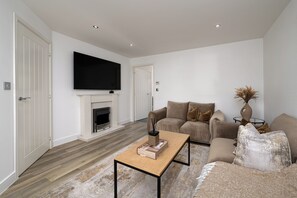 A modern living room with a fireplace, a flat-screen TV mounted above it, a sofa set, and a coffee table. - Chic 4BR Home | Garden | Free Parking | Maidstone (Kent)