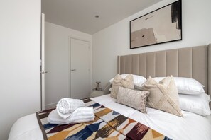 A hotel room with a bed, pillows, a blanket, a painting on the wall, and a door. - Chic 4BR Home | Garden | Free Parking | Maidstone (Kent)