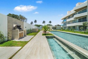 A modern building with a swimming pool, a covered outdoor grill, and a well-maintained lawn. - Beach Escape • Ocean View 1BR at Mareal (Cabarete)
