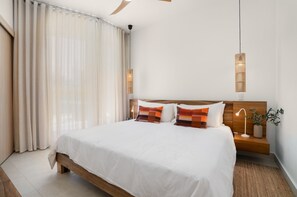 A bedroom with a large bed, wooden headboard, two bedside lamps, and a potted plant. - Beach Escape • Ocean View 1BR at Mareal (Cabarete)