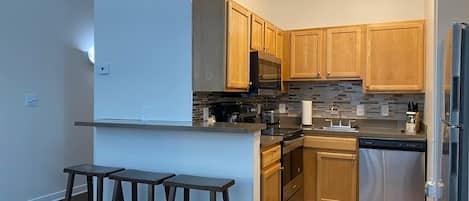 Cocina moderna con armarios de madera, un refrigerador de acero inoxidable y una barra con taburetes.