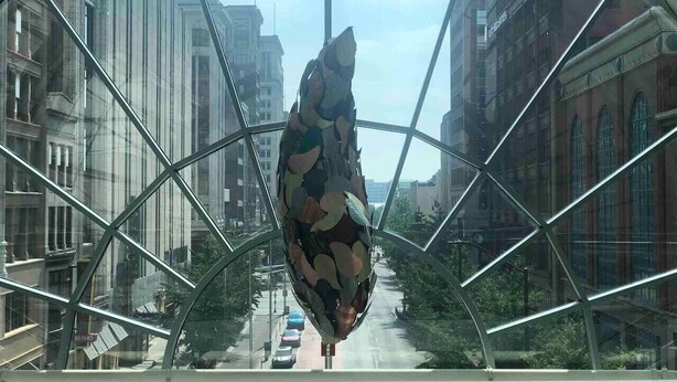 Een grote, geometrische glazen constructie met een vogelbeeld binnenin, omringd door stadsgebouwen.