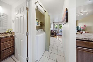 A laundry area with a washing machine, a drying rack, and a shelf with folded towels. - Kihei Bay Vista B102 (Kihei)