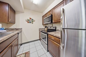 A kitchen with wooden cabinets, a stainless steel refrigerator, a microwave, an oven, and a sink. - Kihei Bay Vista B102 (Kihei)