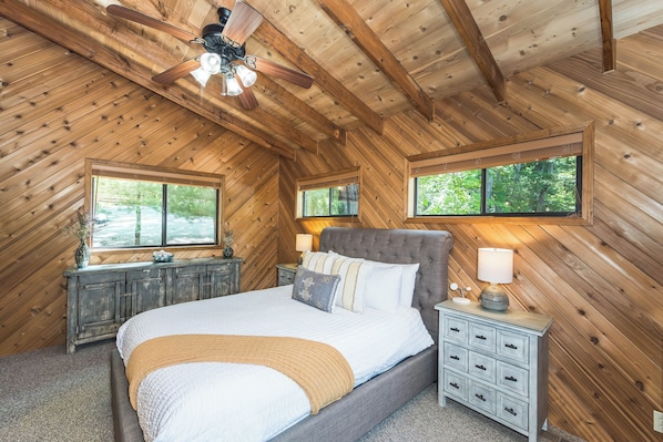 A bedroom with a sloped ceiling, a bed with multiple pillows, a nightstand, and a window. - Longhorn Lakeside Chalet (Beach, Hot Tub, Kayaks) (Innsbrook)