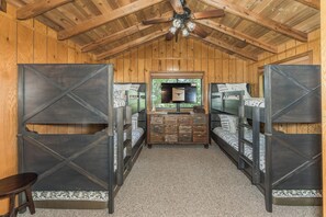A room with bunk beds, a wooden ceiling, and a central dresser with drawers. - Longhorn Lakeside Chalet (Beach, Hot Tub, Kayaks) (Innsbrook)