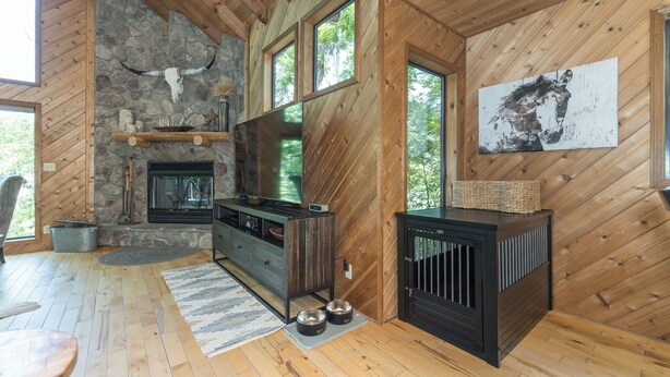Ein Ferienhaus-Interieur mit Kamin aus Stein, Holzwänden, einem großen Fenster und einem aufgehängten Kunstwerk.