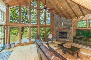 A spacious living room with large windows, a stone fireplace, and a leather sofa. - Longhorn Lakeside Chalet (Beach, Hot Tub, Kayaks) (Innsbrook)