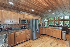 A modern kitchen with wooden cabinets, stainless steel appliances, and a large window providing a view of the outdoors. - Longhorn Lakeside Chalet (Beach, Hot Tub, Kayaks) (Innsbrook)
