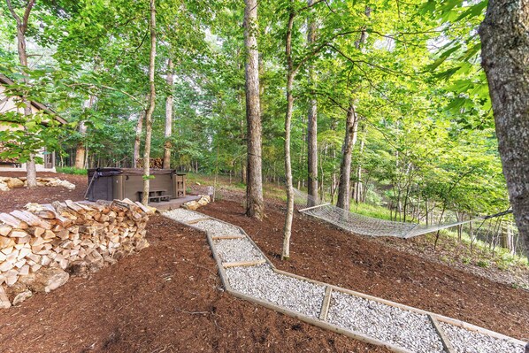 A forested area with a wooden deck, a small cabin, and a gravel path.