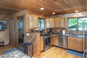 A modern kitchen with wooden cabinetry, stainless steel appliances, and a large window providing a view of the outdoors. - Longhorn Lakeside Chalet (Beach, Hot Tub, Kayaks) (Innsbrook)