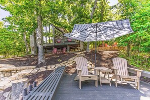 Een terras met Adirondack-stoelen en een tafel, omringd door een stenen muur en bomen.