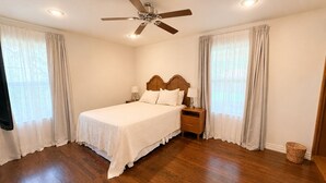 Un dormitorio con una cama de madera, una mesita de noche, un ventilador de techo y una ventana con cortinas.