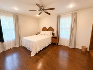 Ein Schlafzimmer mit einem Holzbett, einem Nachttisch, einem Deckenventilator und einem Fenster mit Vorhängen.