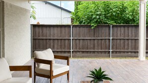 Un patio techado con ventilador de techo, una mesa de madera con planta en maceta y una zona de estar con sofá y sillones acolchados.