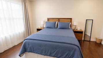 A bedroom with a bed, two bedside tables with lamps, a ceiling fan, a mirror, and a window with curtains.