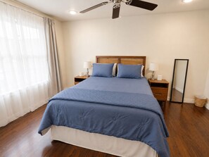 A bedroom with a bed, two bedside tables with lamps, a ceiling fan, a mirror, and a window with curtains.