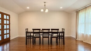 Comedor con mesa y sillas de madera, luces empotradas en el techo y un ventanal con cortinas.
